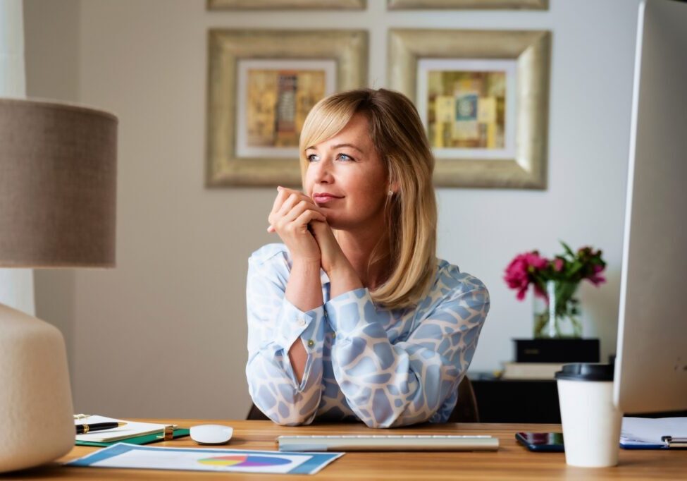 Thinking middle aged woman sitting at desk while working from home